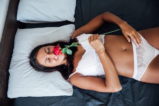 woman in her underwear lies on a bed with a red rose
