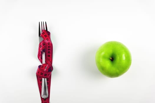 Green apple, fork and measuring tape. Diet concept. Diet for weight loss with a measuring tape and fruit on a white background, top view.