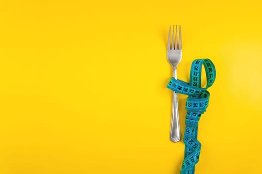 Diet, weight loss and weight loss concept. Fork with measuring tape on yellow background, top view, space for text.