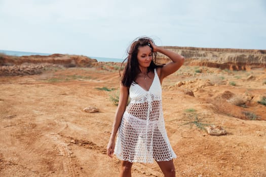 woman in white clothes stands by a sandy mountain