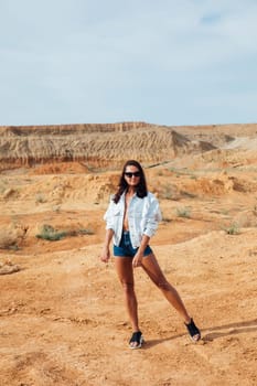 woman in denim shorts stands by a sandy mountain