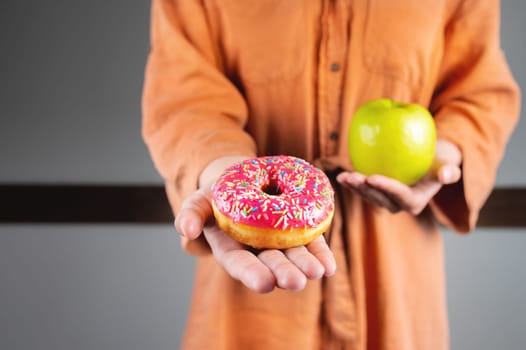 It is difficult to choose a healthy eating concept when a woman is holding a green apple and a donut with a lot of calories in her hand. Unrecognizable girl holding out a donut.