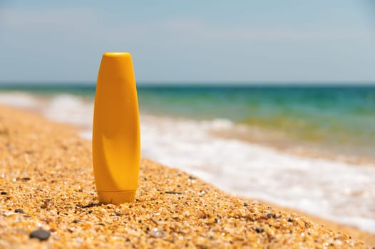 Empty textured sandy beach by the summer sea with a bottle of sun cream. empty cosmetic skincare cream or sunscreen on sandy beach with sea background, leisure and travel accessory.