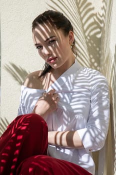 beautiful woman in light clothes sits in the shade of a plant