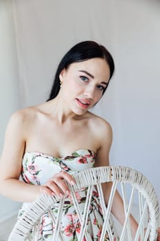 portrait of beautiful brunette woman in a dress by a wicker chair