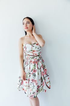 woman in a floral dress stands against a white wall