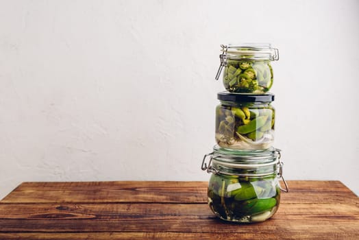 Three Glass Jars of Freshly Canned Jalapeno Peppers with Herbs and Garlic on Wooden Table. Copy Space