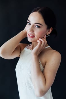 brunette woman in light clothes poses on a black background