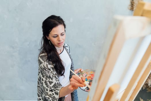 a female artist draws with a brush using a palette on an easel in an art studio teacher training