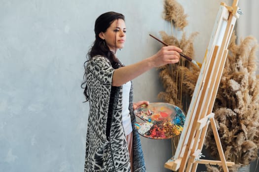 a female artist draws with a brush using a palette on an easel in an art studio teacher training