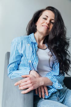 brunette woman in denim sitting in a chair in a room