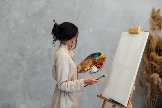 artist stands with a palette and brushes at the easel