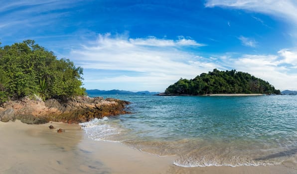 A tranquil tropical beach featuring clear waters, a sandy shore, a vibrant green island, and a blue sky.