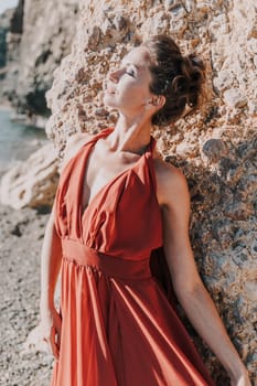 Woman red dress sea. Woman in a long red dress posing on a beach with rocks on sunny day. Girl on the nature on blue sky background