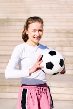 portrait of a smiling sports woman in a concrete soccer court with a ball in her hands, concept of football lifestyle and urban sport in the city