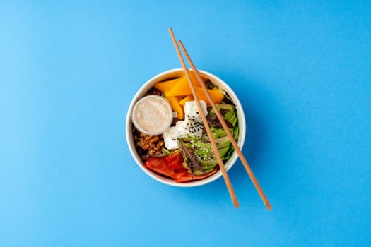 Top view of fresh poke bowl on blue background in studio