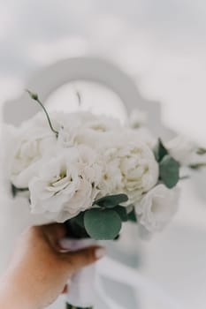 A bouquet of white flowers with green leaves is being held by a person's hand. The arrangement is simple and elegant, with the white flowers providing a clean and fresh look