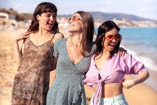 Cheerful multiethnic friends with sunglasses happy on vacation on the beach, looking at the camera.