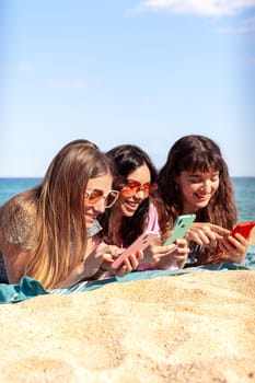 Group of smiling multiethnic women enjoying vacation. Beautiful and cheerful Gen Z girls with their mobile phones pose looking at the camera with a mobile phone.