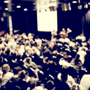 Business and entrepreneurship symposium. Speaker giving a talk at business meeting. Audience in conference hall. Rear view of unrecognized participant in audience.