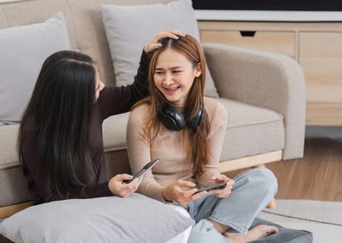 Lesbian and LGBT couple sitting together in a cozy living room, smiling and using smartphones, enjoying a relaxed and happy moment.