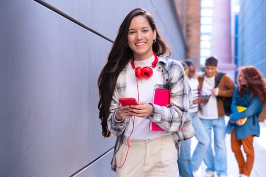 Young smiling student with notebook in hand uses social networks with smartphone applications and wireless technology outdoors.