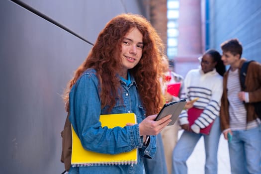 Young smiling student with notebook in hand uses social networks with smartphone applications and wireless technology outdoors.