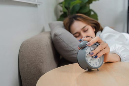 A young woman turns off her alarm clock in the morning, beginning her day in a cozy and relaxed home setting.