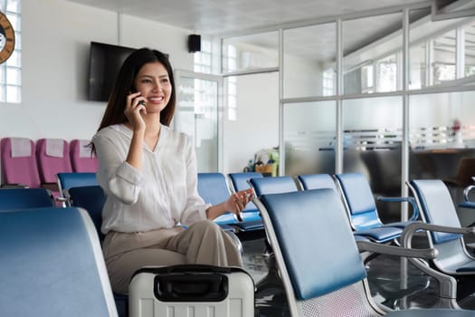 A woman sits in an airport lounge, smiling while talking on her phone and holding a boarding pass, ready to board her flight.