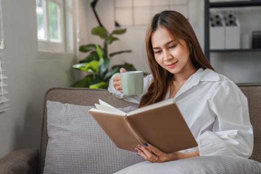 A young woman starts her day with a relaxing morning routine, enjoying a cup of coffee and reading a book in a cozy, modern living room.