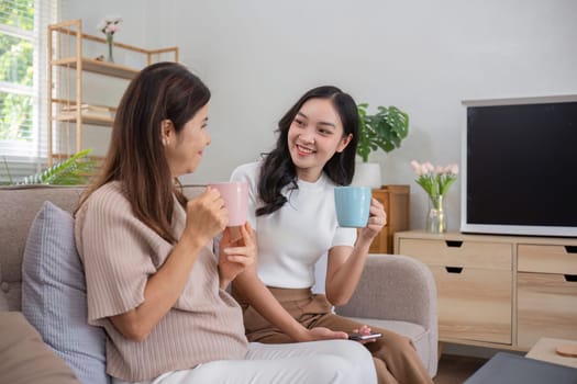 An elderly mother and her adult daughter spend quality time together, enjoying coffee and conversations in a cozy living room setting.