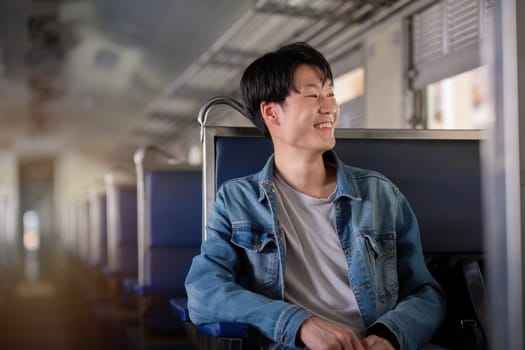 A young man sits on a train, smiling and looking out the window. He wears a casual denim jacket, creating a relaxed travel atmosphere.