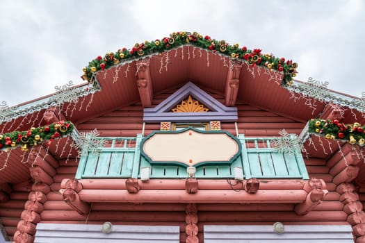 This photo shows the exterior of a log cabin building adorned with Christmas decorations, including garlands of evergreen branches, red and gold ornaments, and snowflakes.