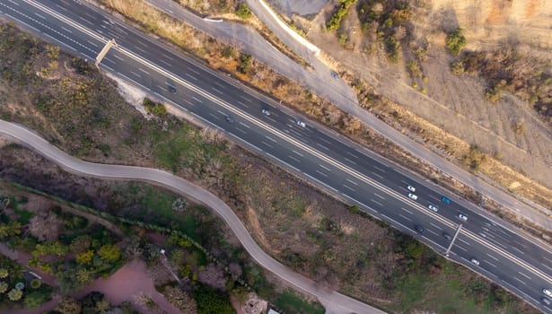 An aerial view of a highway winding through a forest, with asphalt road surface surrounded by trees and natural landscape.
