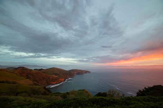 A beautiful sunset over the ocean with a cloudy sky. The sky is orange and pink, and the water is calm. The scene is serene and peaceful, and it evokes a sense of calmness and relaxation