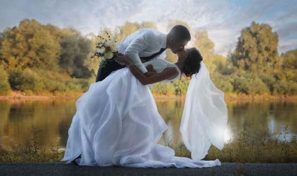 The groom kisses his bride against the background of the river in the rays of the setting sun. High quality photo