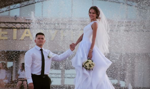 Bride and groom holding hands against the background of a fountain. High quality photo