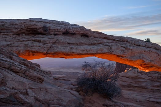 Sunrise at Famous Mesa Arch in Canyonlands National Park, Utah. The warm morning light illuminates the red rocks, creating a mesmerizing glow - USA