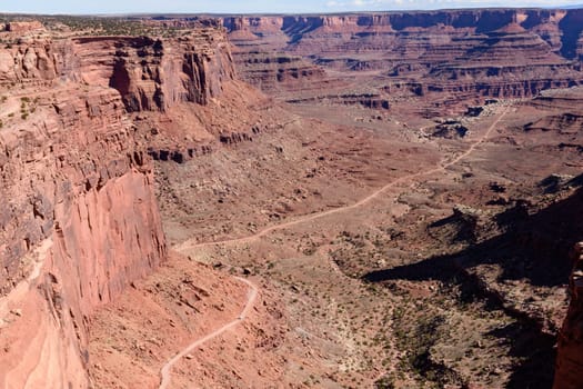A stunning distant shot of the Shafer Trail road winding through the breathtaking red rock landscape of Canyonlands National Park in Utah, USA. The image captures the rugged beauty of the terrain.