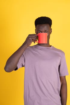A man in a tan shirt is holding a red coffee cup and looking at the camera. Concept of casualness and relaxation, as the man is enjoying a hot beverage while posing for the camera