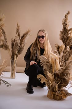 A woman photographer, a blonde with a camera, seriously with sunglasses in the production studio. Wearing a black clothes on a brown background