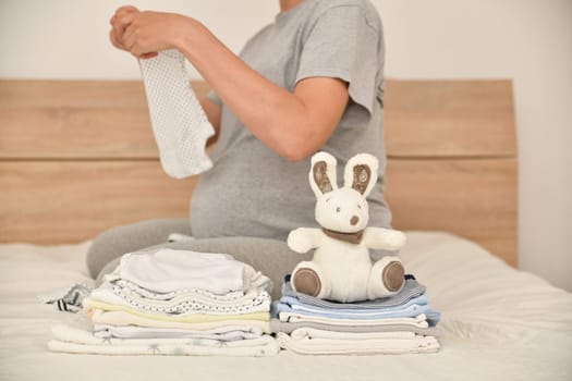 Pile of baby clothes with a rabbit and pregnant woman