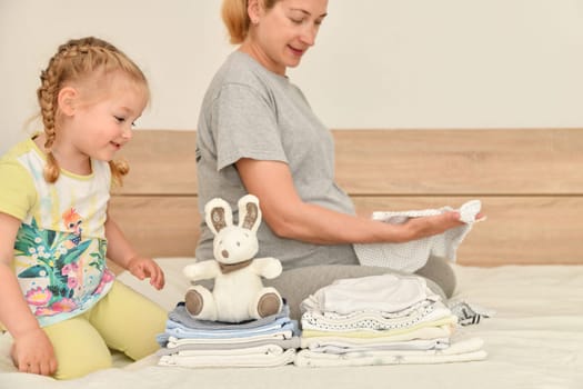Mother and daughter together prepare clothes for a newborn boy