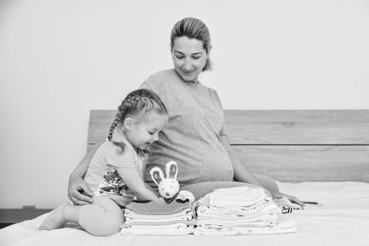 Mother and daughter together prepare clothes for a newborn boy