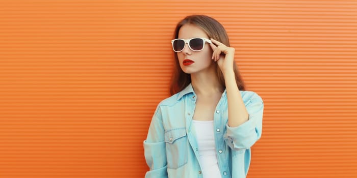 Portrait of modern stylish young woman in white glasses, casual clothing posing on vivid orange wall background