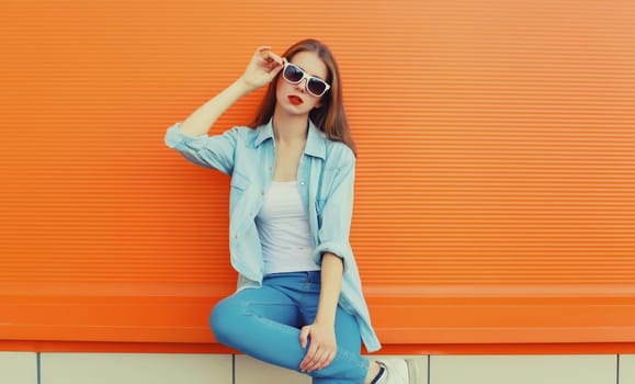Portrait of modern stylish young woman in white glasses, casual clothing posing on vivid orange wall background