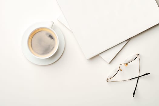 Blank paper, coffee cup and glasses on white desk from above