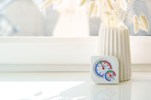 A white windowsill with dried flowers in a white vase and a glass vase.