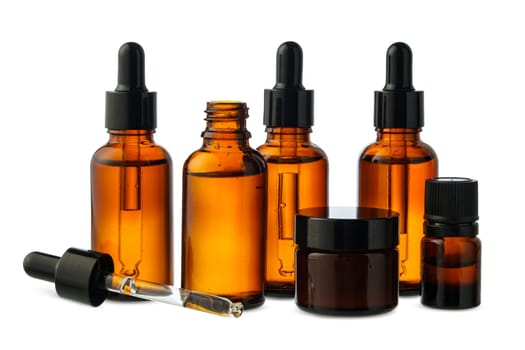 A group of amber glass bottles of essential oils and a cream jar are arranged on a white background.
