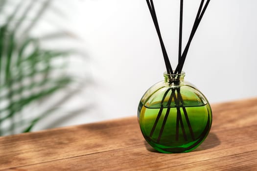 A green glass reed diffuser with black reeds sits on a wooden tabletop.
